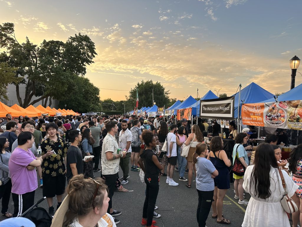 Vibrant Queens Market with bustling stalls, shoppers, and colorful displays.